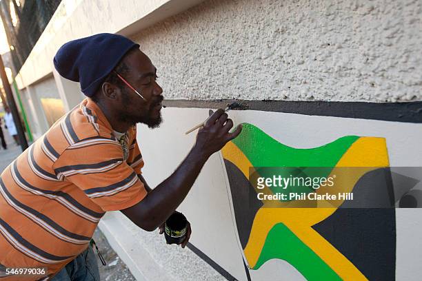 Rastafarian man painting a Jamaican flag on a wall, Kingston.