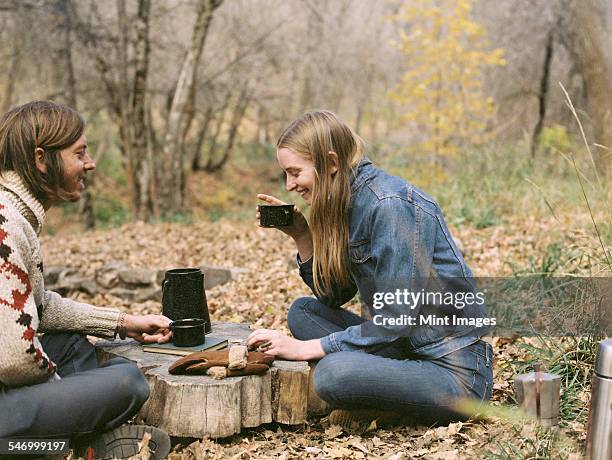 smiling couple sitting on the ground in a forest, drinking coffee. - stump stock pictures, royalty-free photos & images