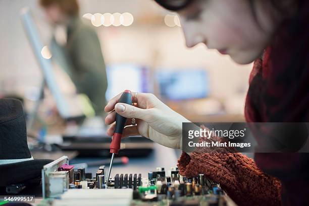 Computer Repair Shop. A woman using an electronic screwdriver tool on a computer circuit board.