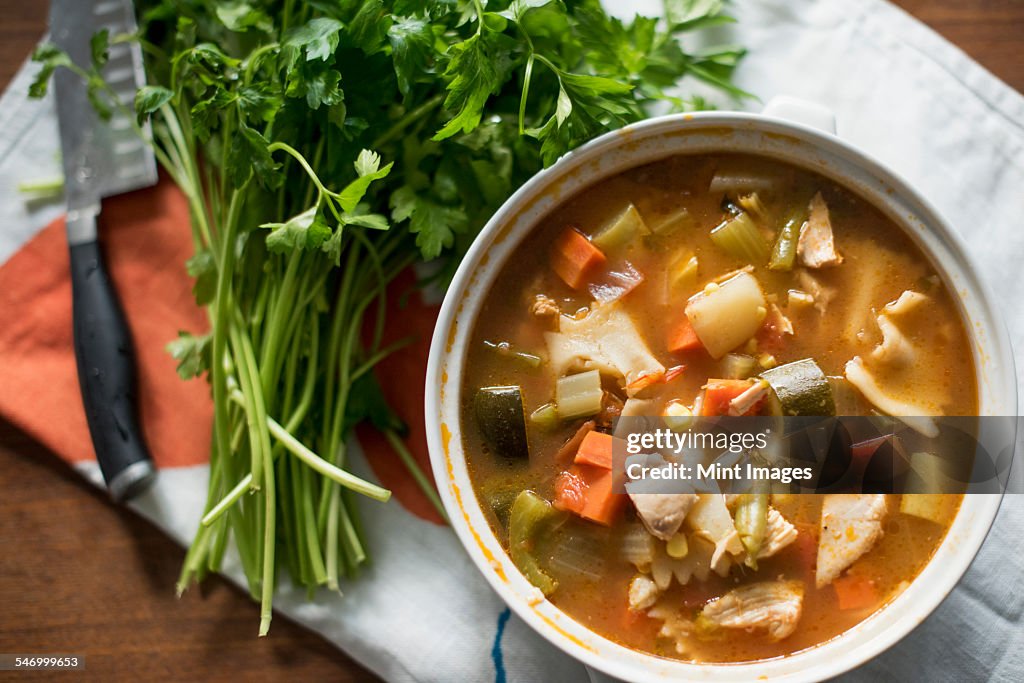 A bowl of vegetable stew and a bunch of fresh herbs on a table.