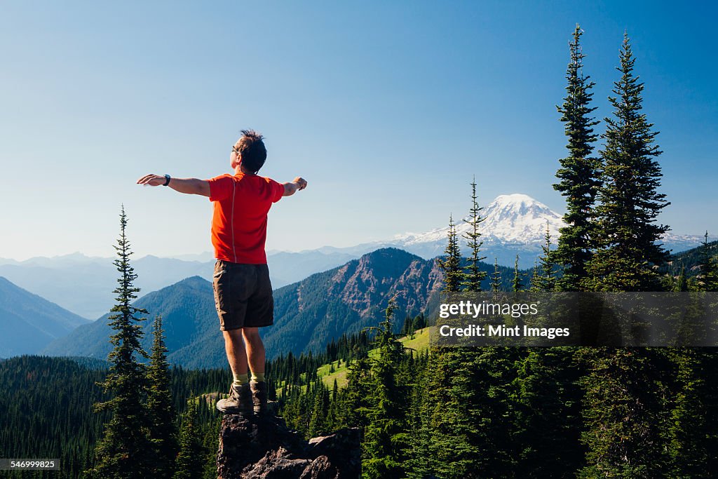 Male hiker standing with his arms outstretched on a mountain top, looking over the landscape.