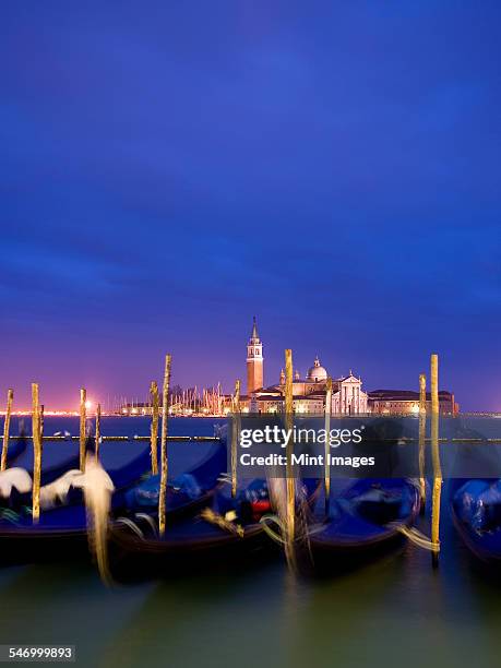 a view from the riva degli schiavoni and the piazza san marco across the water to the island and church of san giorgio maggiore. gondolas moored at dusk. - gondola traditional boat foto e immagini stock