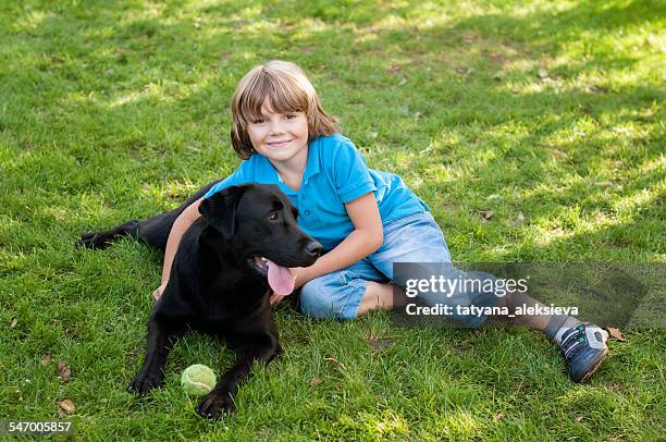 boy (6-7) lying on lawn with dog - black labrador with ball stock pictures, royalty-free photos & images