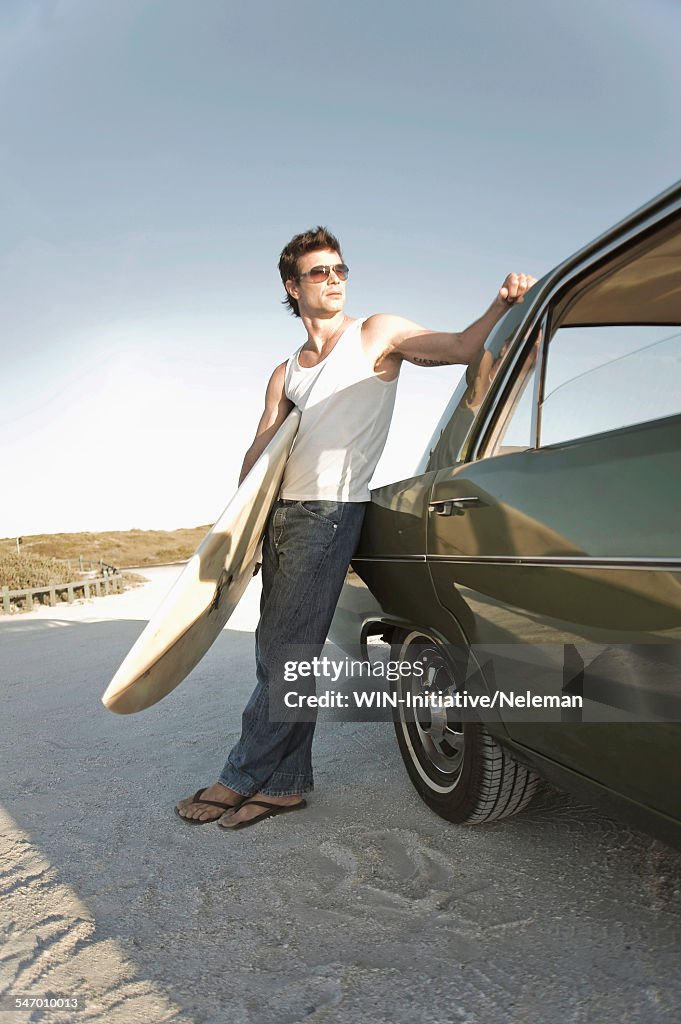 Man standing near a car and holding a surfboard