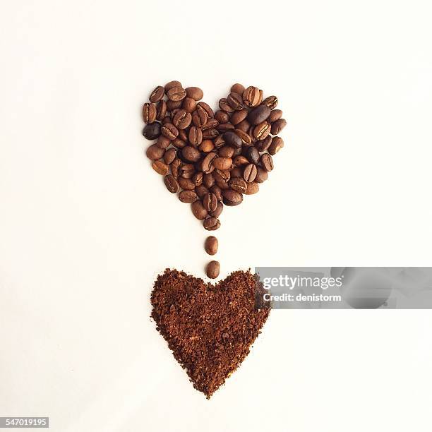 coffee beans in a heart shape, dripping into another heart shape of ground coffee - coffee powder stock-fotos und bilder