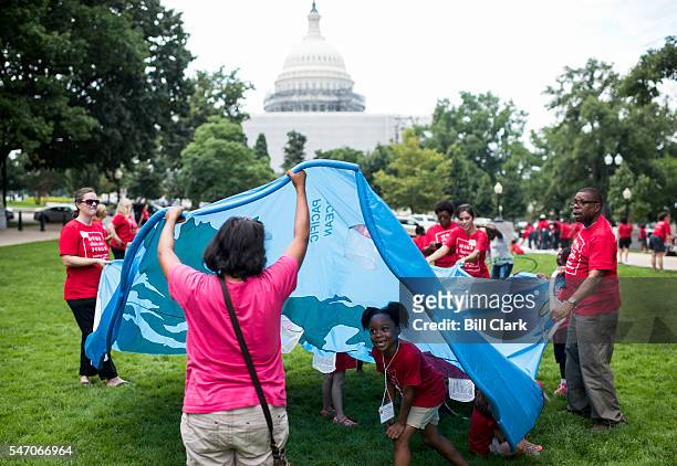 Kids play under a fabric map of the world during the Moms Clean Air Force "play-in for climate action" in Upper Senate Park on Wednesday, July 13,...