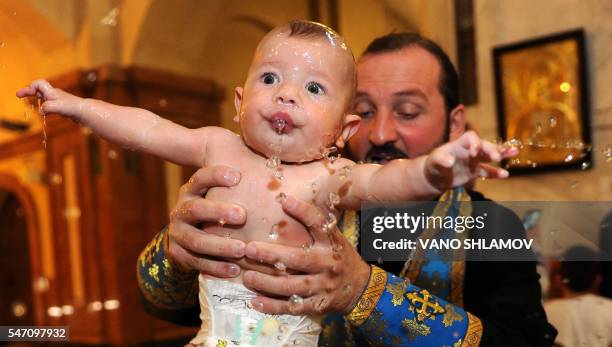 Georgian Orthodox priest baptises a baby during a mass baptism ceremony at the Holy Trinity Cathedral in Tbilisi, on July 13, 2016.