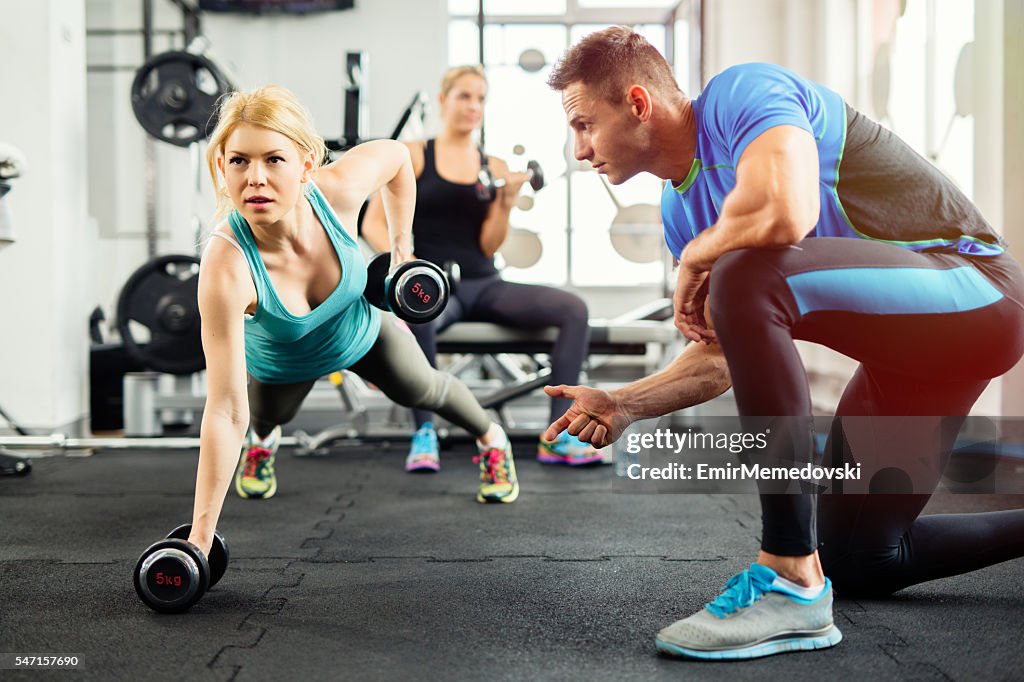 Sportliche Frau, die Push-ups unter Aufsicht von Personal Trainer.