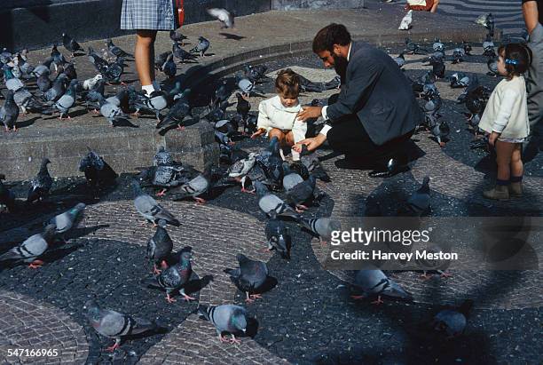 Man and children feeding pigeons at the port in Lisbon, Portugal, circa 1960.