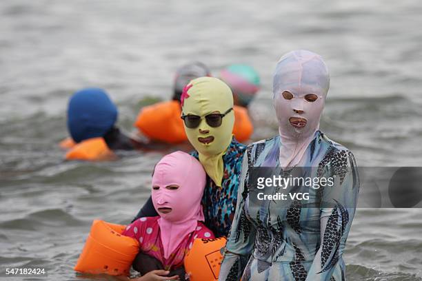 Visitors wear facekinis while posing in water on July 13, 2016 in Qingdao, Shandong Province of China. Facekini is originally designed from diving...