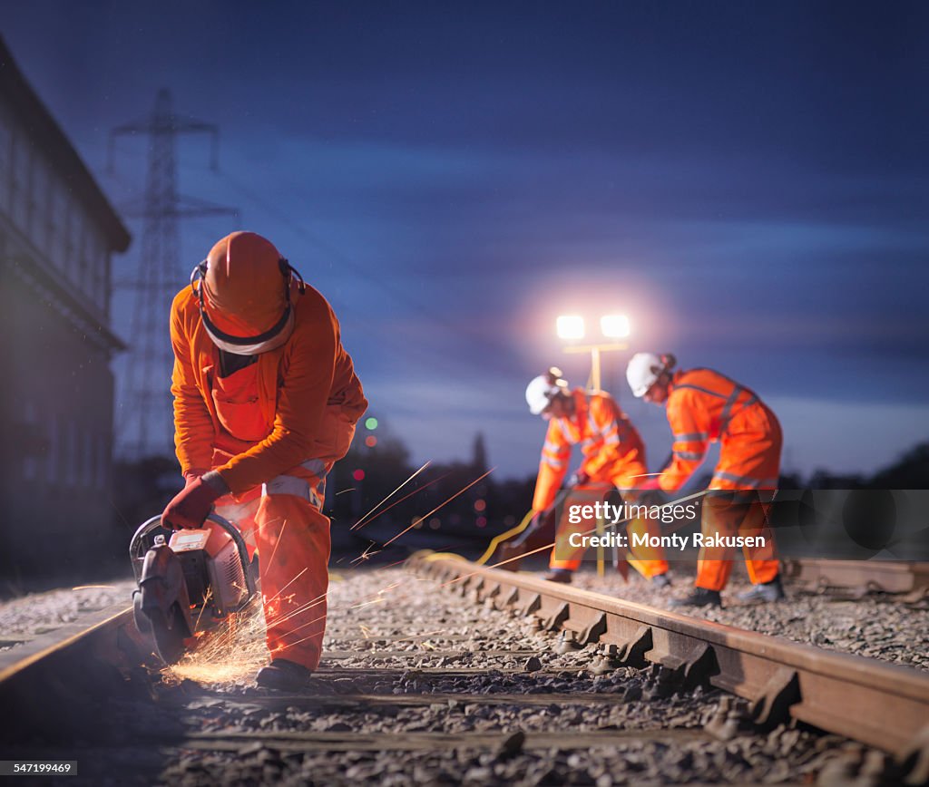 Railway maintenance workers using grinder on track at night