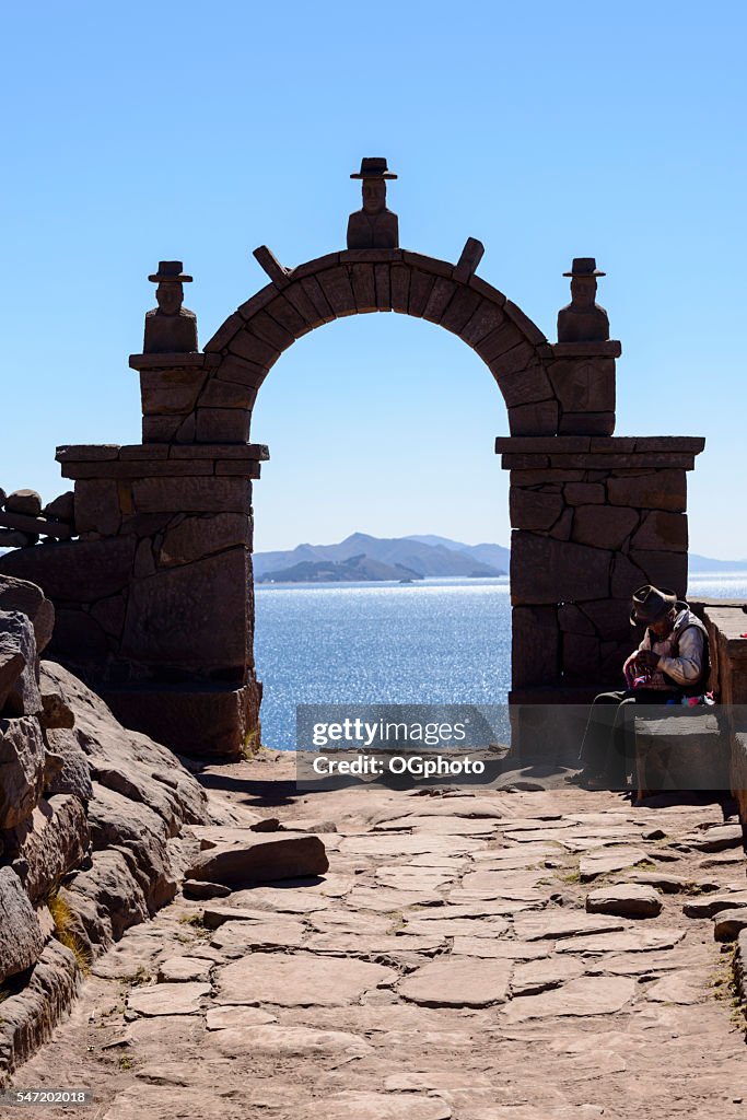 Idoso tricotando ao lado de um arco de pedra