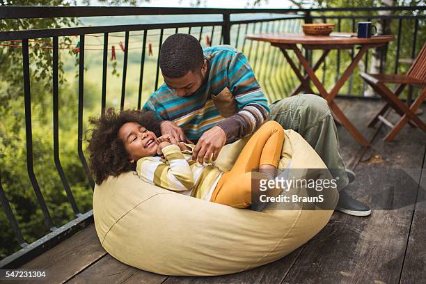 afroamerikanischer vater und tochter, die sich auf einer terrasse amüsen. - bean bag stock-fotos und bilder