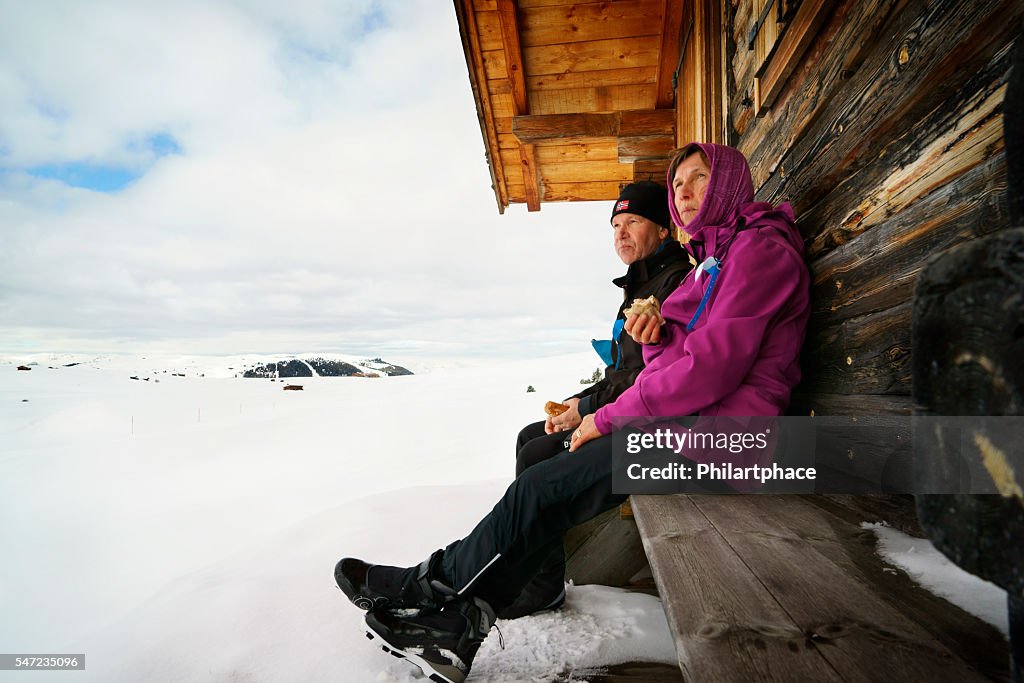 Mature couple resting on bench in snow covered winter landscape