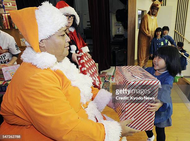 Japan - Konishiki , a Hawaiian-born sumo wrestler-turned-TV personality, dressed up as Santa Claus, gives a present to a girl in Higashimatsushima,...