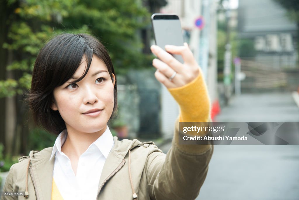 Asian woman taking photograph of herself with mobi