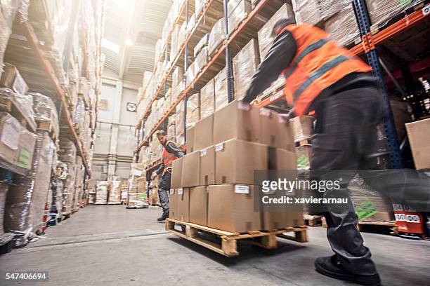 motion blur of two men moving boxes in a warehouse - dringendheid stockfoto's en -beelden