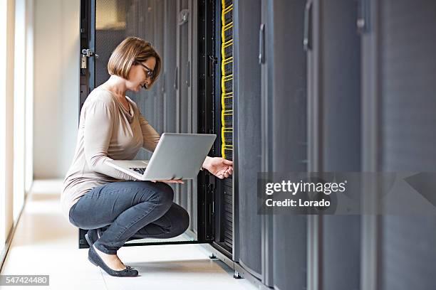 attractive brunette adult female employee working in internet server room - data storage stockfoto's en -beelden
