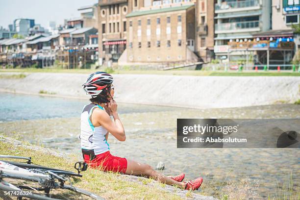 japanese female bicycle rider resting by kamo river, kyoto, japan - kamo river stock pictures, royalty-free photos & images