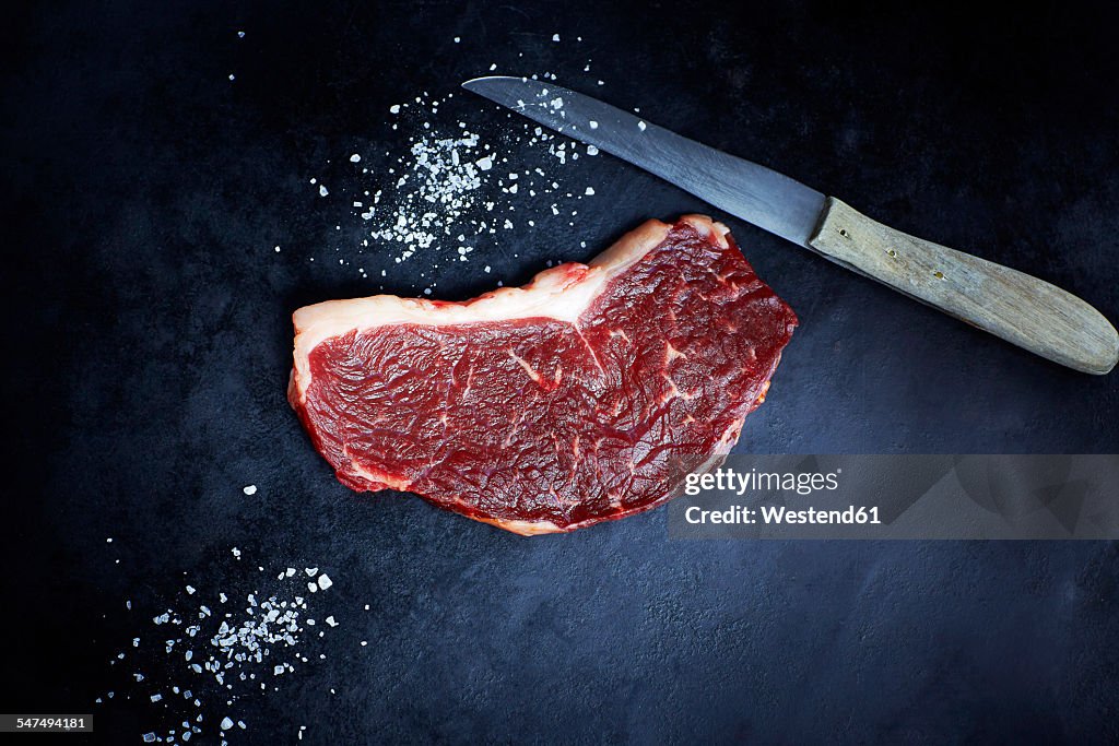 Raw striploin steak, salt and knife