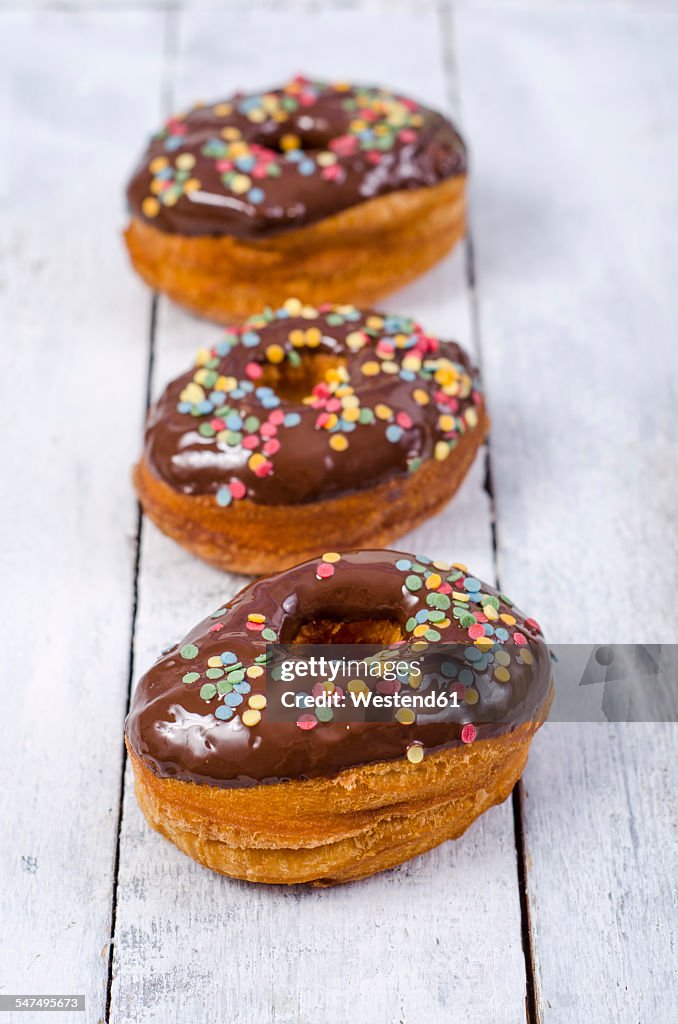 Row of three American cronuts with chocolate icing and sugar confetti