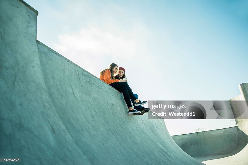 Two teenage girls in skatepark sharing cell phone
