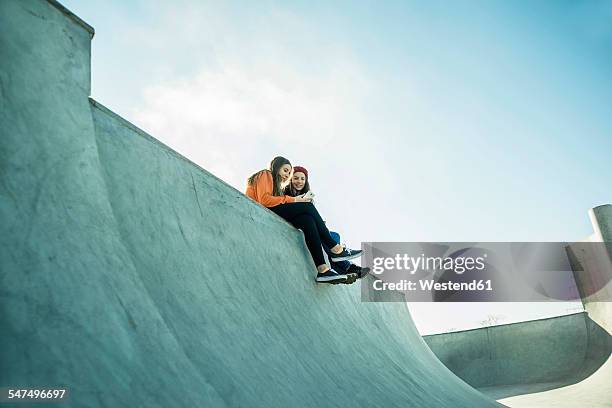 two teenage girls in skatepark sharing cell phone - hip friends stock pictures, royalty-free photos & images