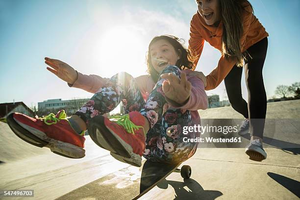 teenage girl pushing girl on skateboard - kind vor der pubertät stock-fotos und bilder