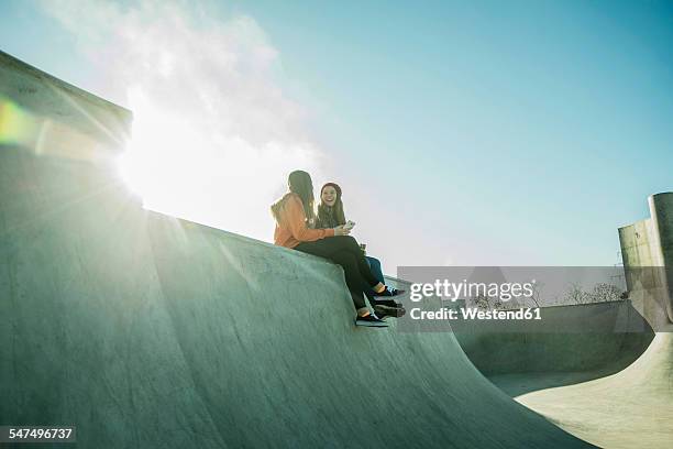 two teenage girls in skatepark sharing cell phone - blue sky friends stock pictures, royalty-free photos & images