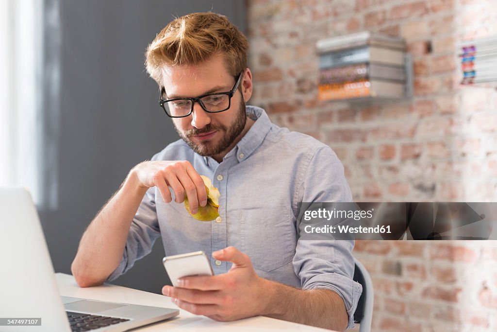 Young man at desk with cell phone and laptop