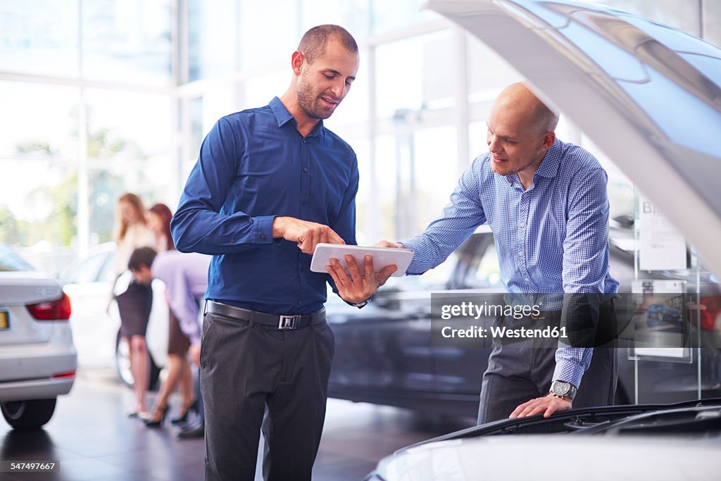 Two men at car dealer with digital tablet