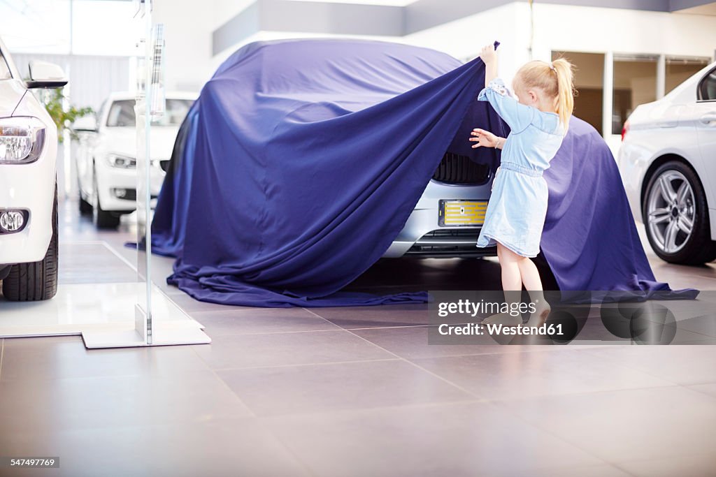 Girl at car dealer unveiling tarpaulin