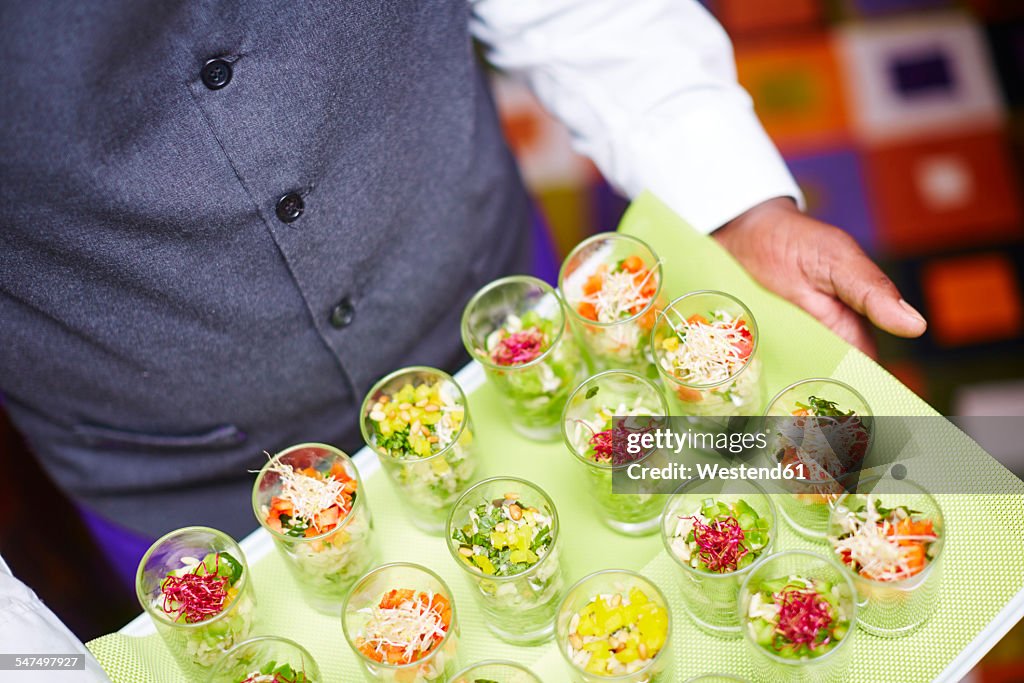 Waiter carrying tray of individual salads in glasses