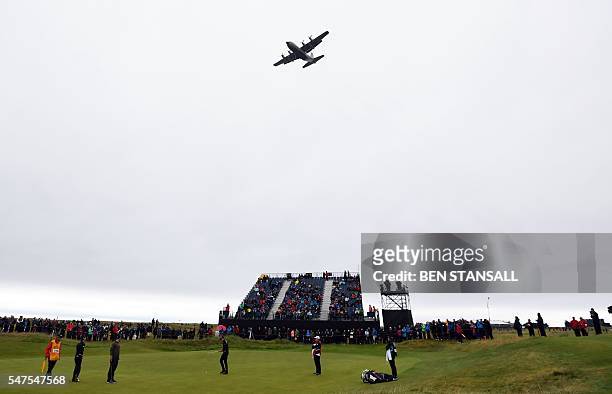Lockheed C-130 Hercules flies over the 15th green as Sweden's Henrik Stenson, US golfer Zach Johnson and Australia's Adam Scott putt during their...