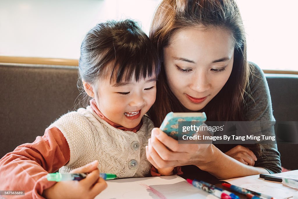 Mom using smartphone with daughter in restaurant