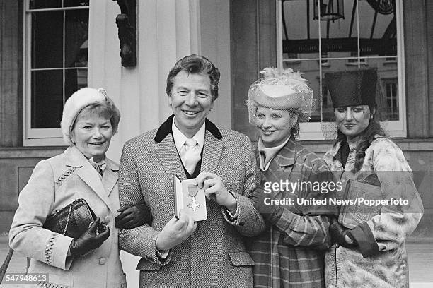 English comedian, singer and actor Max Bygraves pictured holding his OBE award with his wife Gladys and daughters at an investiture ceremony at...