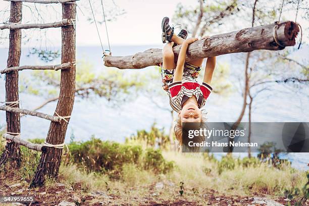 boy hanging upside down on tree trunk - schommelen bungelen stockfoto's en -beelden