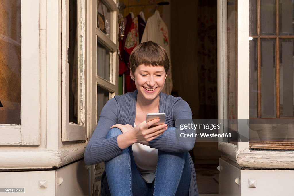 Portrait of female fashion designer with smartphone sitting at the entrance of her studio