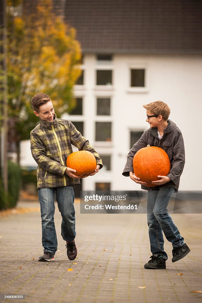 Two boys carrying two big pumpkins