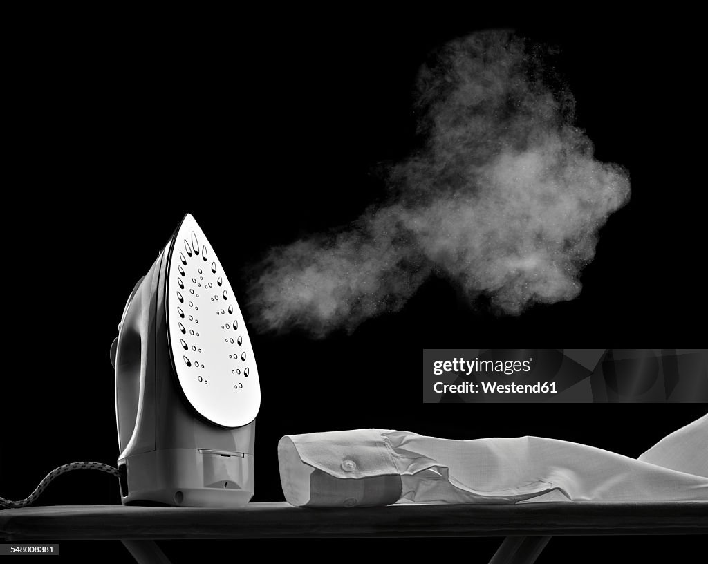 Steaming flat iron and shirt sleeve in front of black background