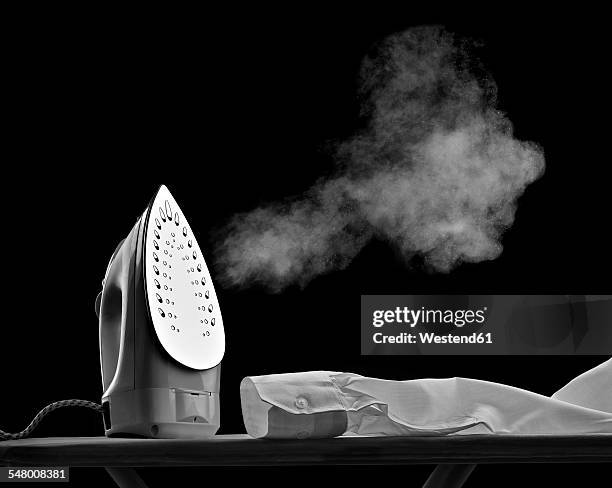 steaming flat iron and shirt sleeve in front of black background - iron stock pictures, royalty-free photos & images