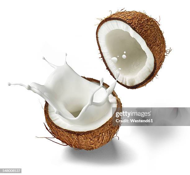 two halves of a coconut and splashing coconut milk in front of white background - kokosnuss stock-fotos und bilder