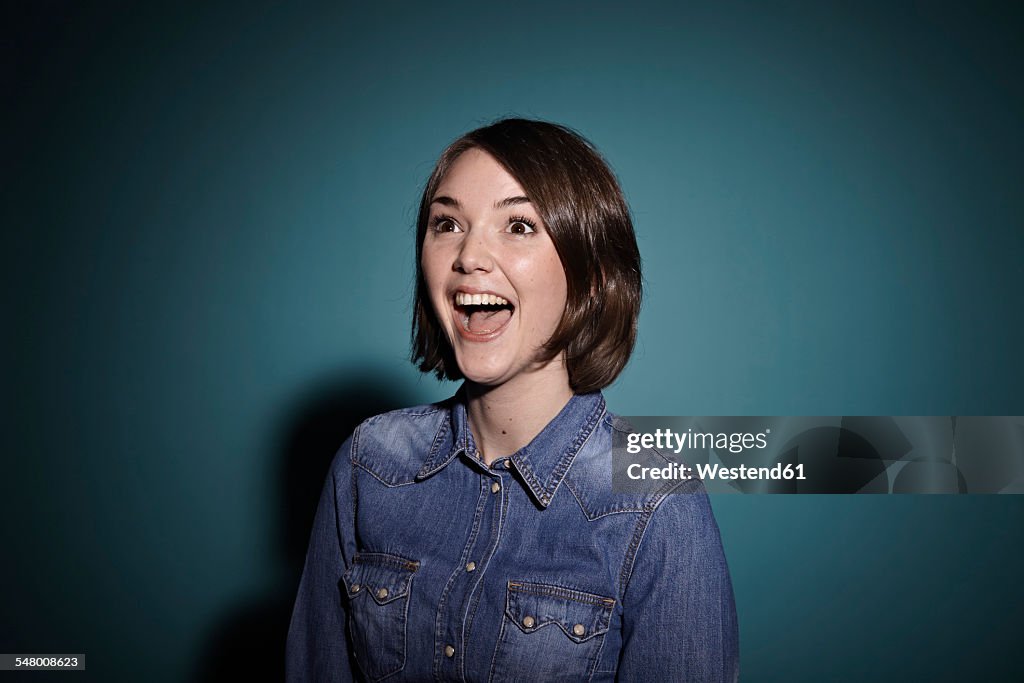 Portrait of astonished young woman in front of blue background