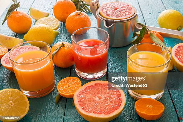 glasses of orange juice, grapefruit juice and multivitamine juice, juice squeezer and fruits on wood - fruit juice stock pictures, royalty-free photos & images