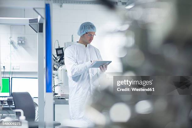 technician in cleanroom holding digital tablet - cleanroom stock-fotos und bilder