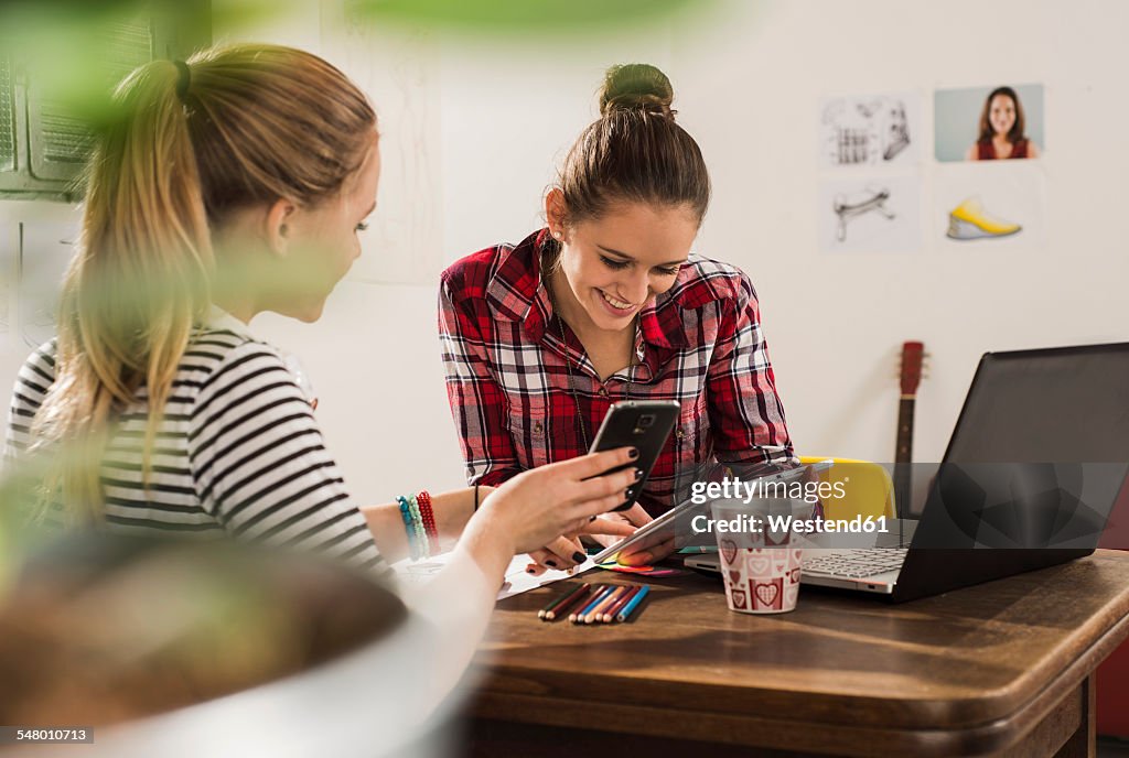 Two female friends with smartphone, laptop and digital tablet at home