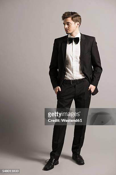 young man with hands in his pockets wearing black suit, white shirt and bow - formal portrait stock-fotos und bilder