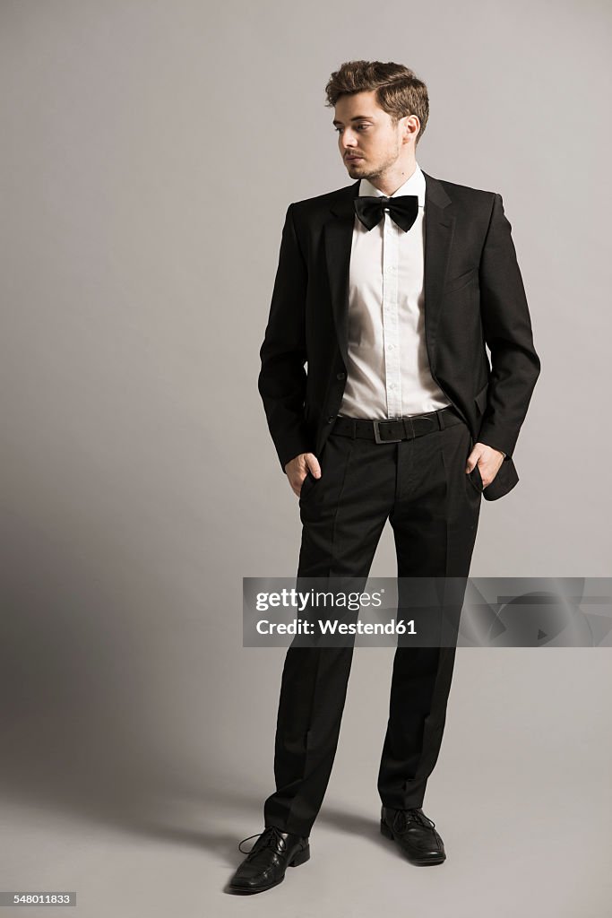 Young man with hands in his pockets wearing black suit, white shirt and bow