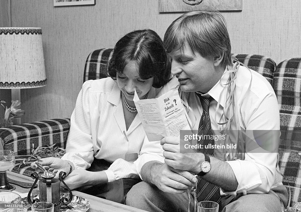 People, night of New Years Eve, celebrating New Years, symbolic, soothsay, lead-pouring, young couple sitting on a couch, woman holds a spoon containing plumb over a lighted candle, aged 25 to 40 years -