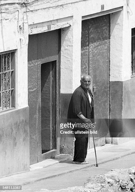People, older people, older man with a walking stick stands in front of a house door, barefooted, aged 70 to 80 years, Spain, Valencia -